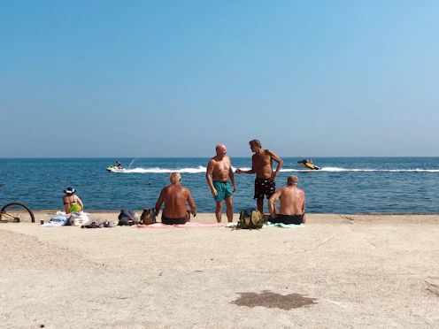 3 women and 2 men sitting on beach sand during daytime