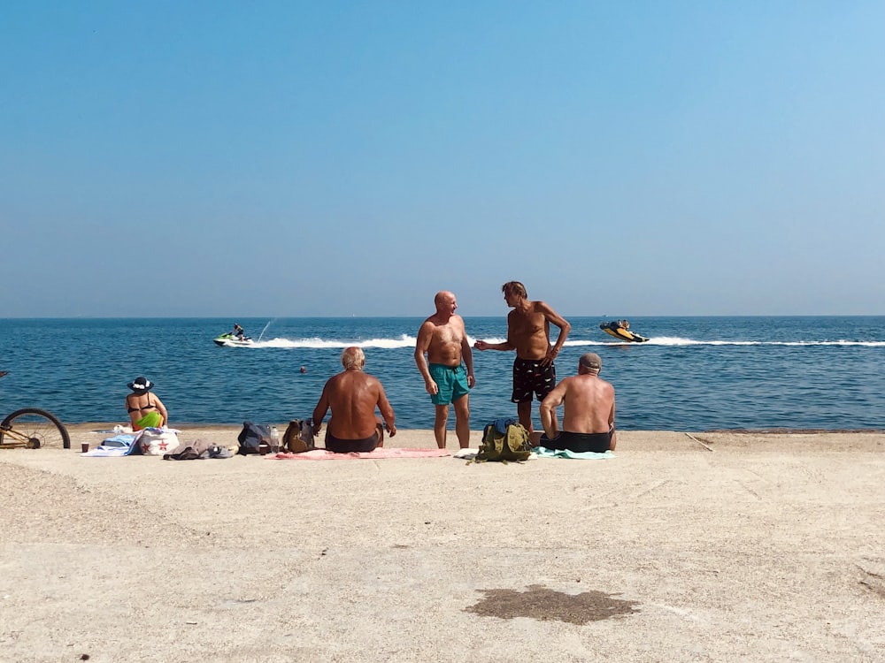 3 mulheres e 2 homens sentados na areia da praia durante o dia