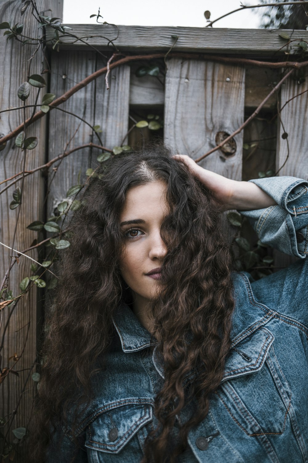 woman in blue denim jacket standing near brown wooden fence