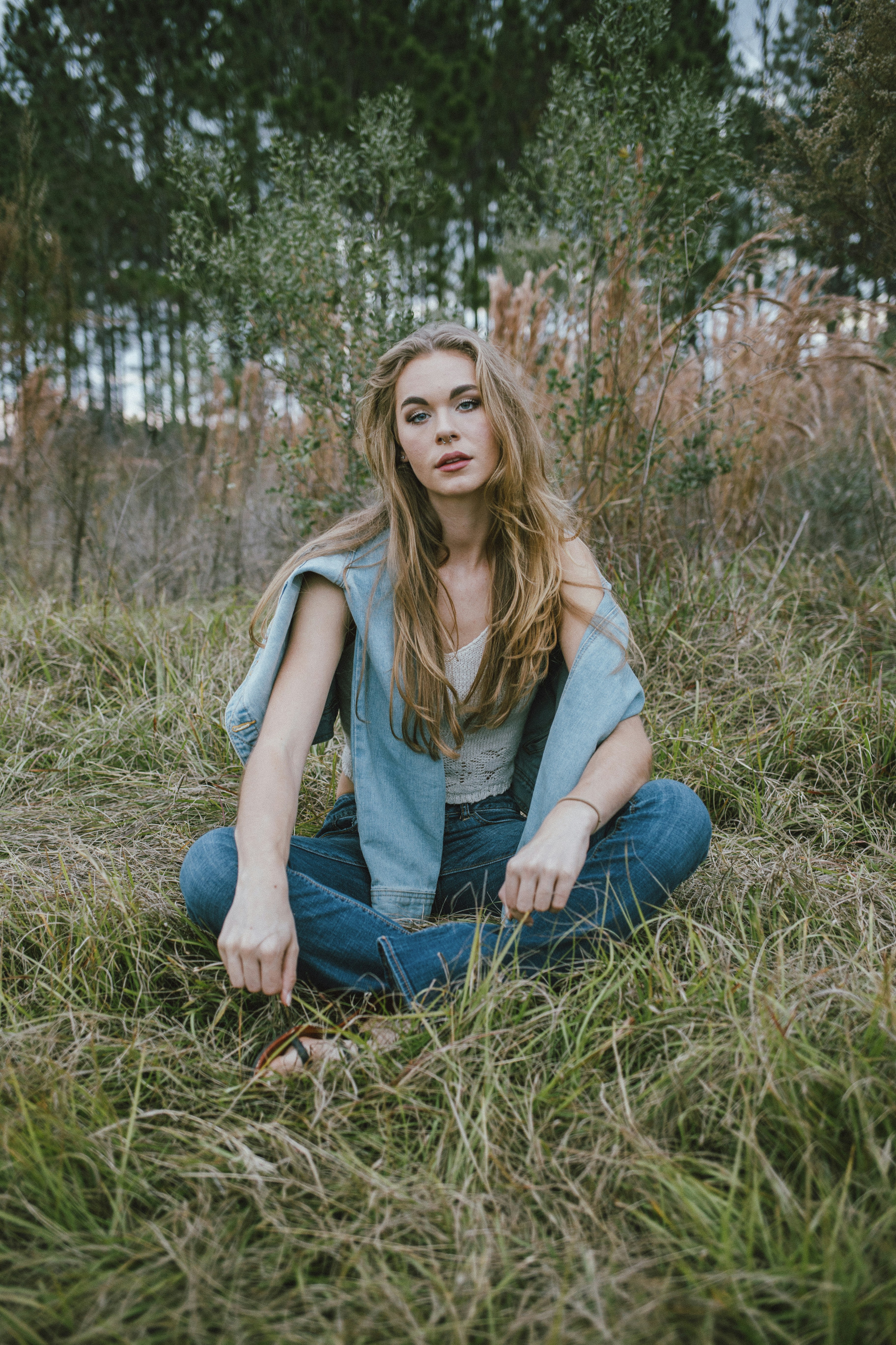 woman in gray tank top and blue denim jeans sitting on brown grass during daytime