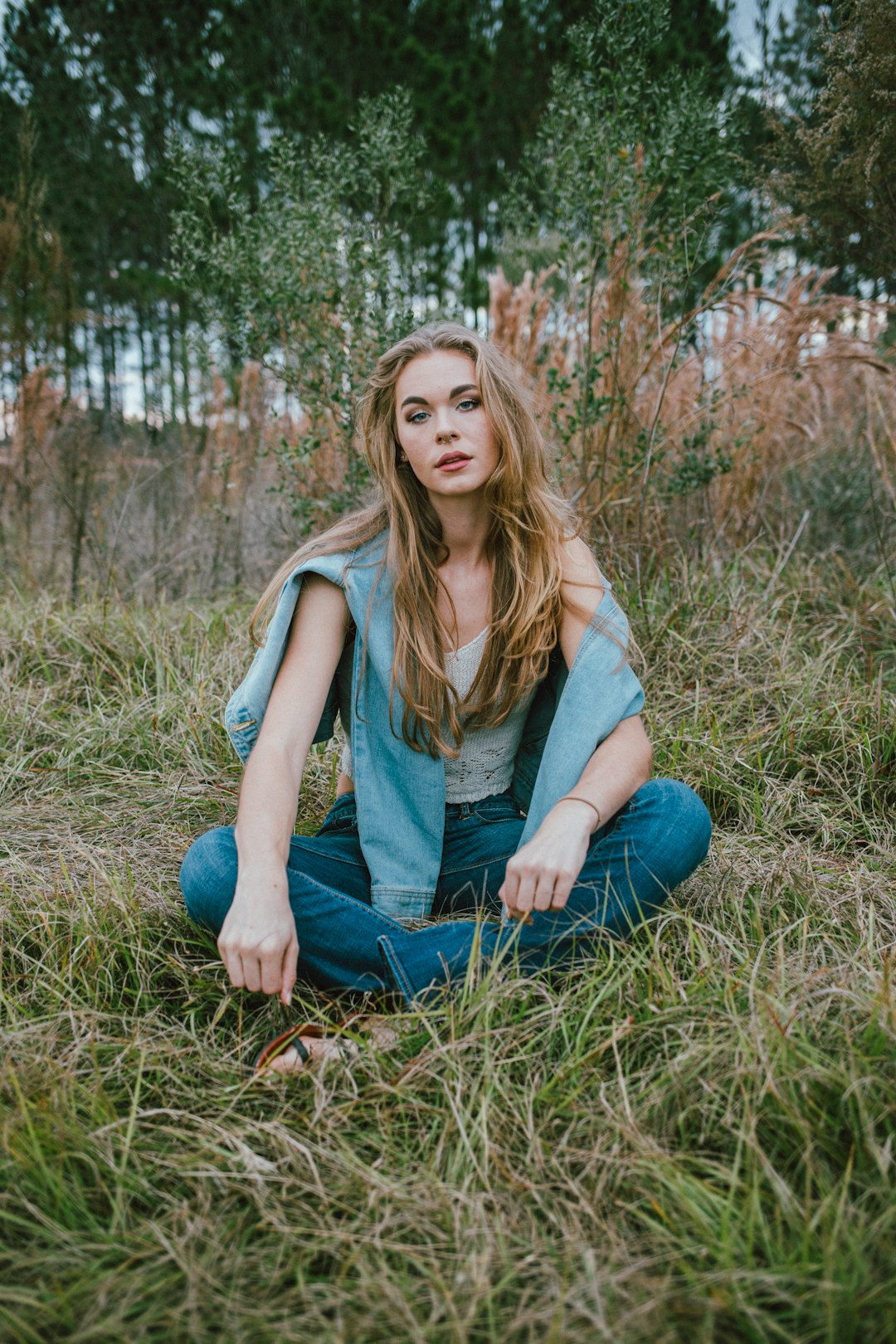 woman in gray tank top and blue denim jeans sitting on brown grass during daytime