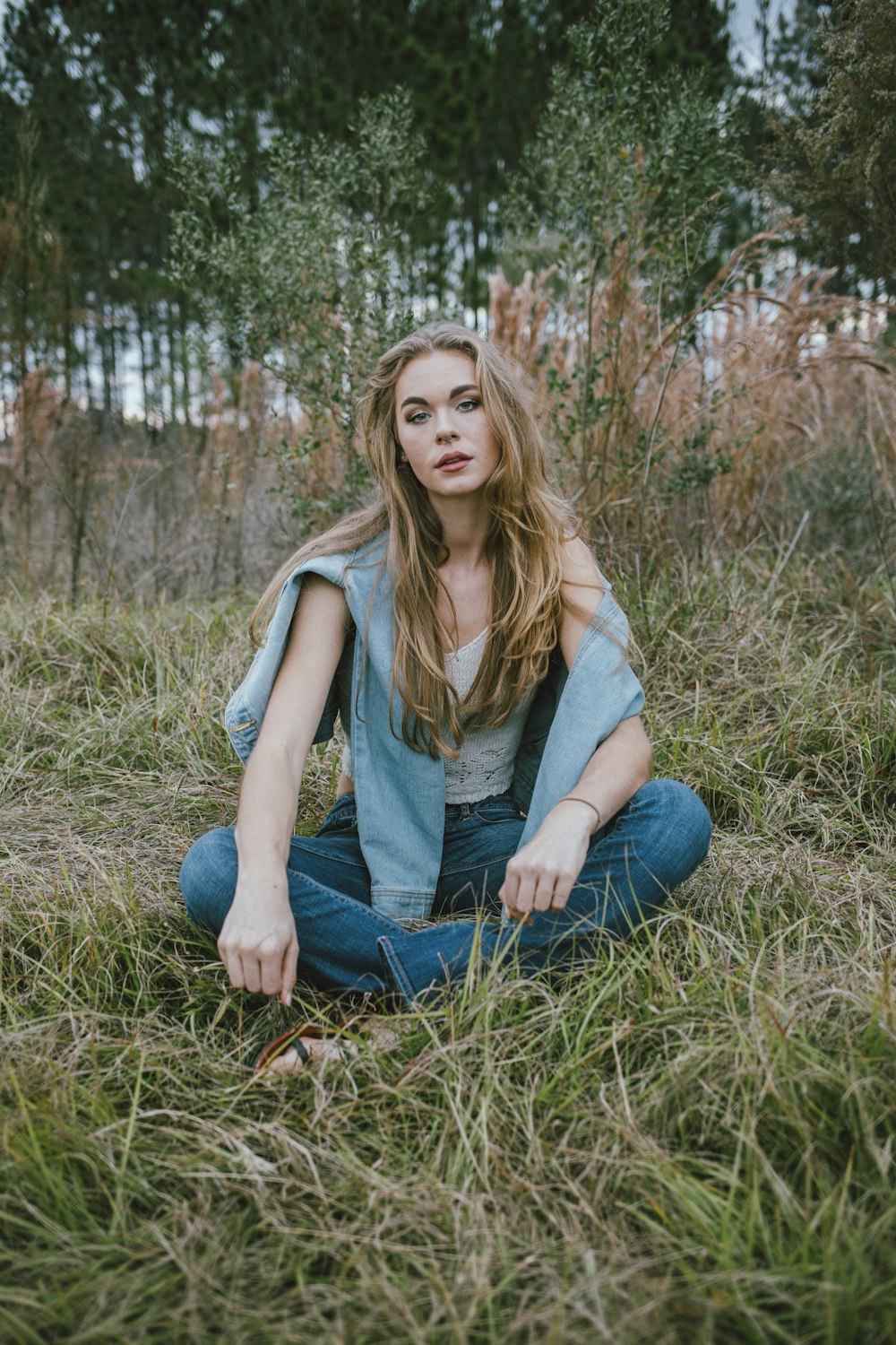 woman in gray tank top and blue denim jeans sitting on brown grass during daytime
