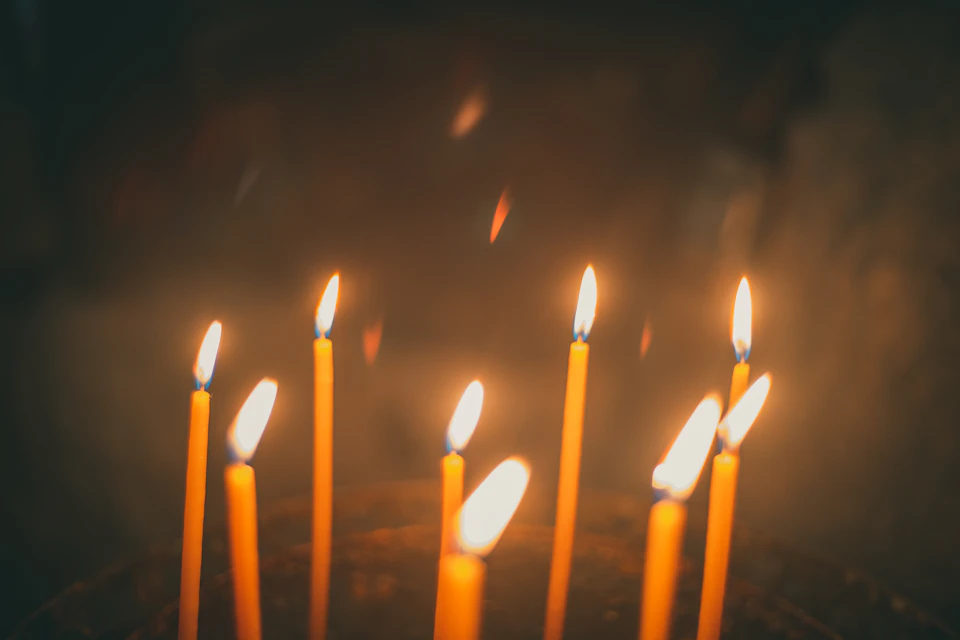 The image shows a group of nine candles, each with its own flame dancing brightly against the dark background. The candles are arranged in three rows of three, creating an aesthetically pleasing pattern that draws the viewer's attention to their warm glow and soft shadows.