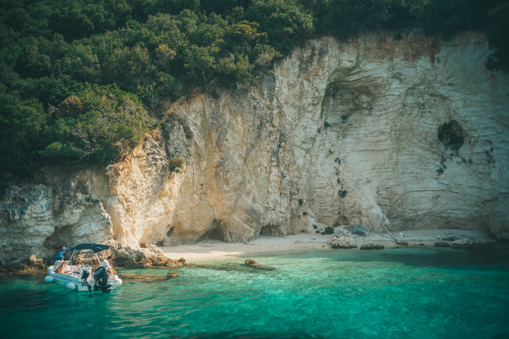 Personas que viajan en bote en el mar cerca de Brown Rocky Mountain durante el día