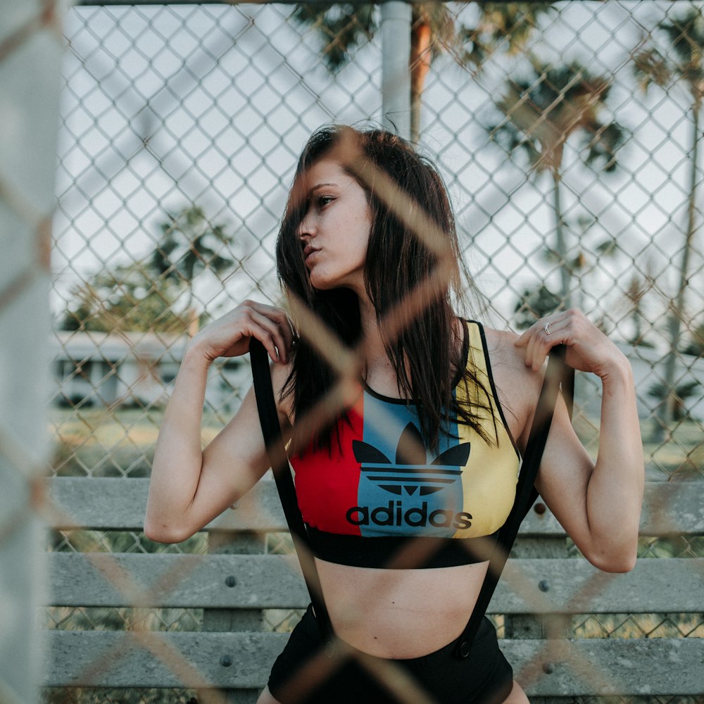 woman in black and red sports bra and black shorts leaning on chain link fence