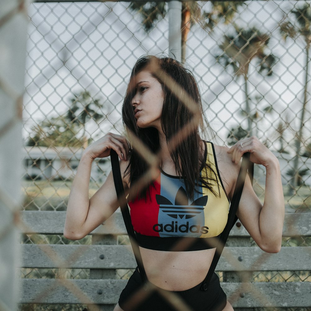woman in black and red sports bra and black shorts leaning on chain link fence
