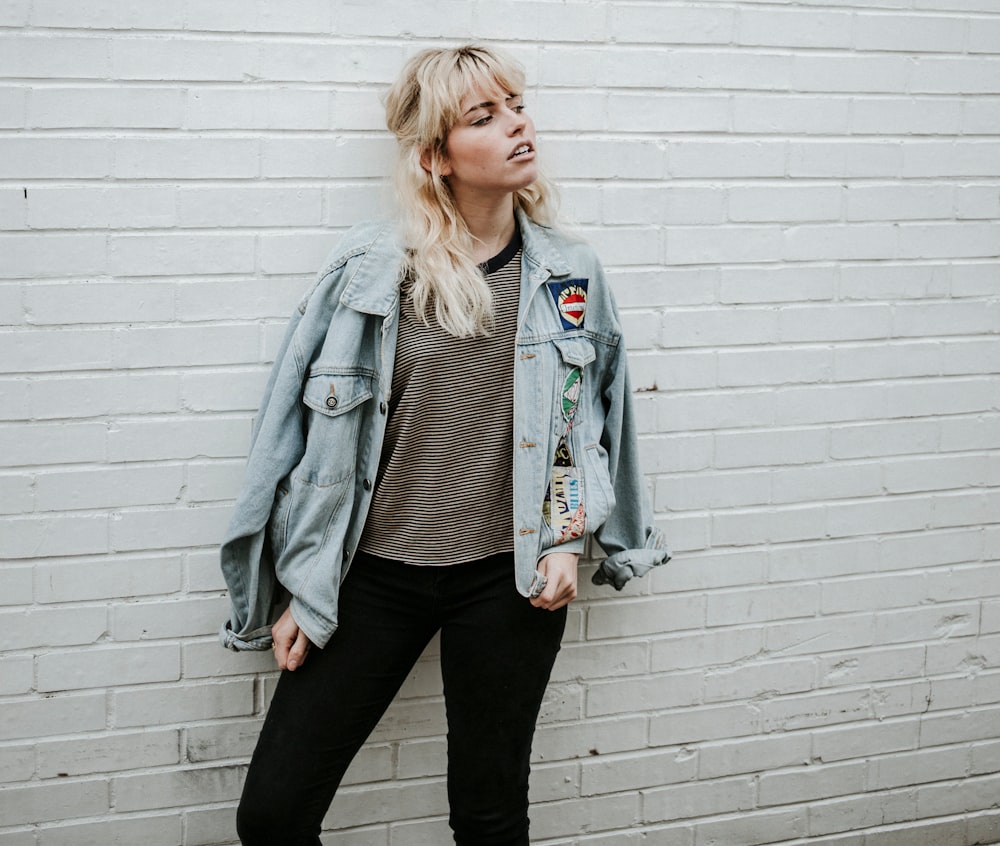 woman in blue denim jacket and black pants standing beside gray wall