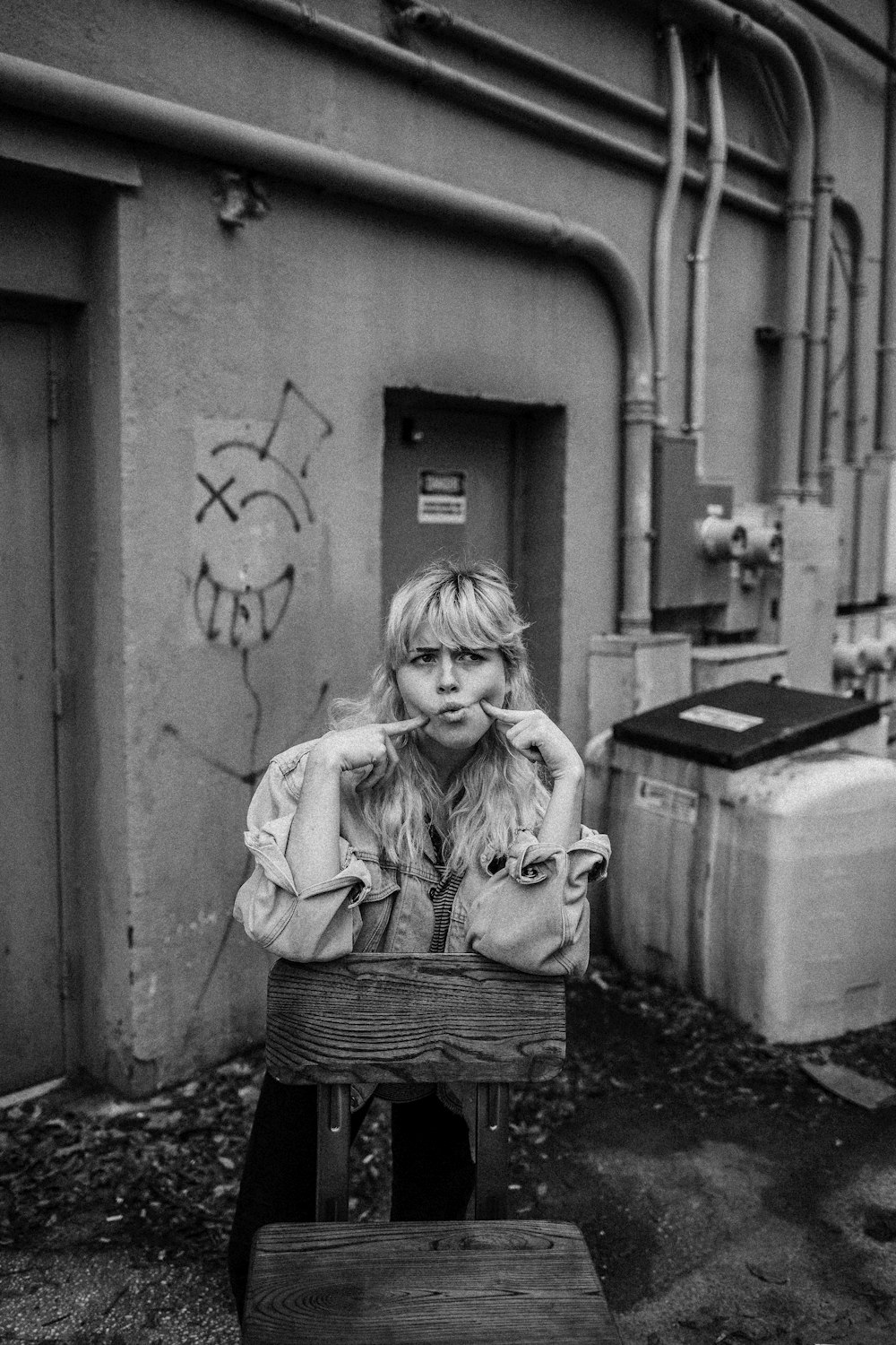 grayscale photo of girl in jacket standing beside wall