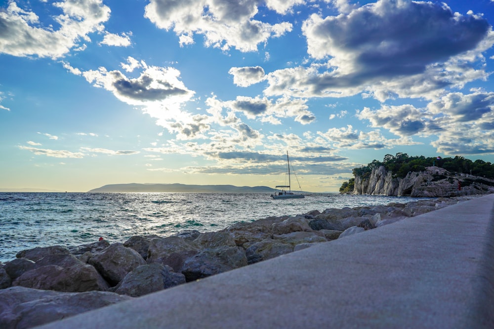 gray rocks near body of water under blue sky and white clouds during daytime