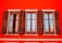 A vibrant red building facade with three adjacent wooden windows that are partially open. The windows have shutters, and elegant wrought iron railings are visible below each window, adding character to the classic architectural design.