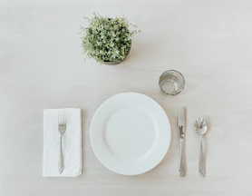white ceramic plate beside stainless steel fork and bread knife on white table