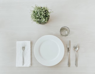 white ceramic plate beside stainless steel fork and bread knife on white table