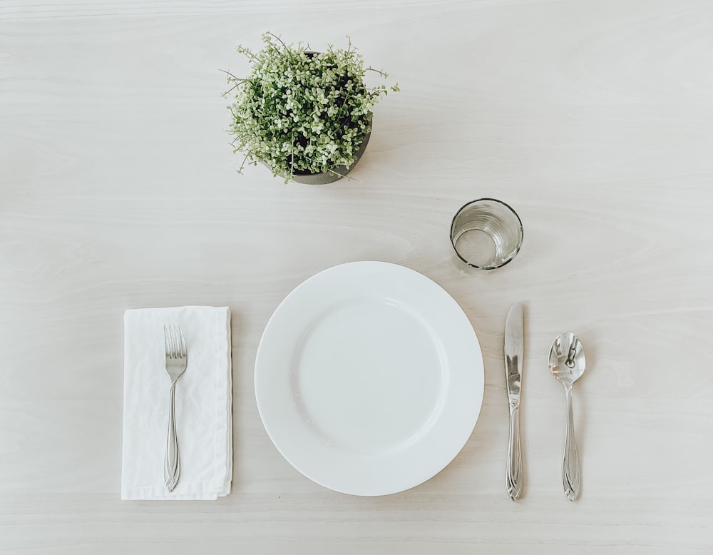 piatto in ceramica bianca accanto a forchetta in acciaio inossidabile e coltello da pane su tavolo bianco