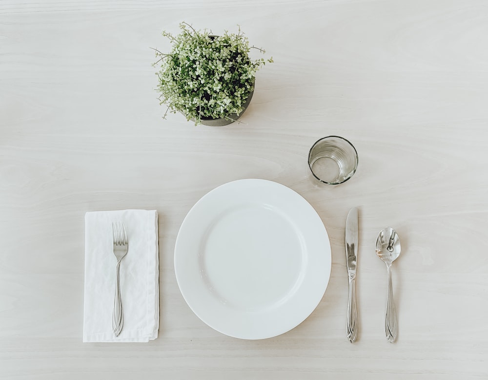 Assiette en céramique blanche à côté d’une fourchette en acier inoxydable et d’un couteau à pain sur une table blanche