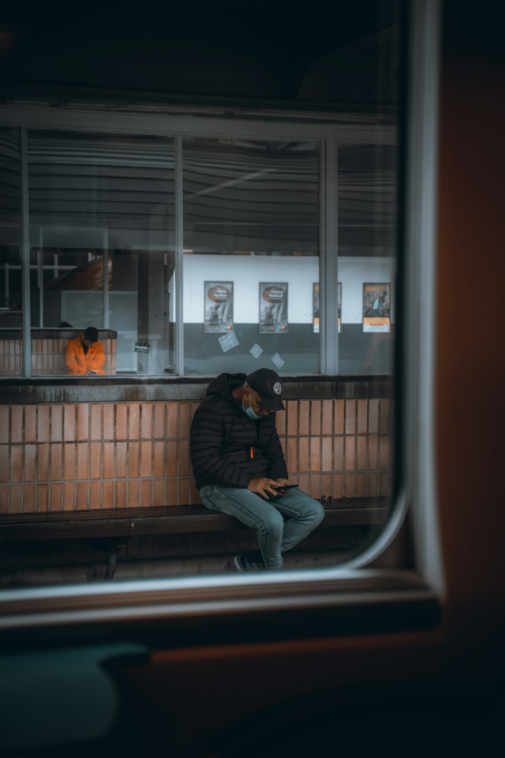 Hombre con chaqueta negra y jeans de mezclilla azules sentado en la ventana