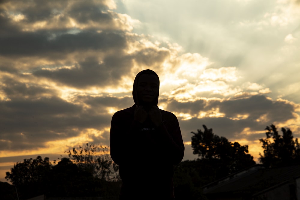 silhouette of man standing near trees under cloudy sky during sunset