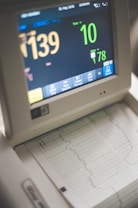 A medical monitor displaying various vital signs including heart rate and pulse. The screen shows numbers like 139 and 78, with graphical representations of the data below on a printout. The device has several buttons for interaction at the bottom.