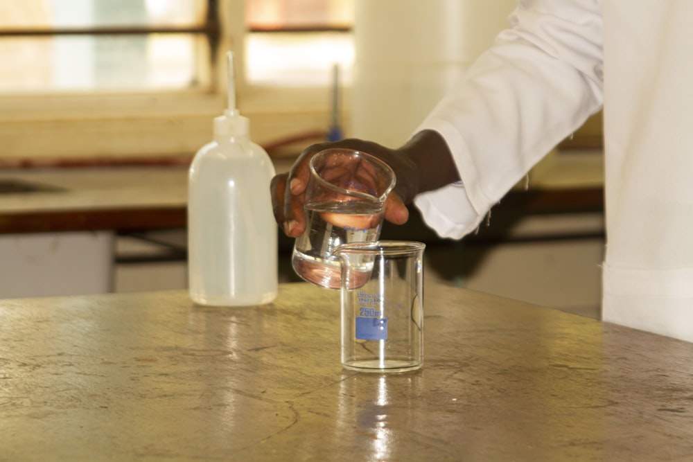 person in white long sleeve shirt holding clear glass bottle