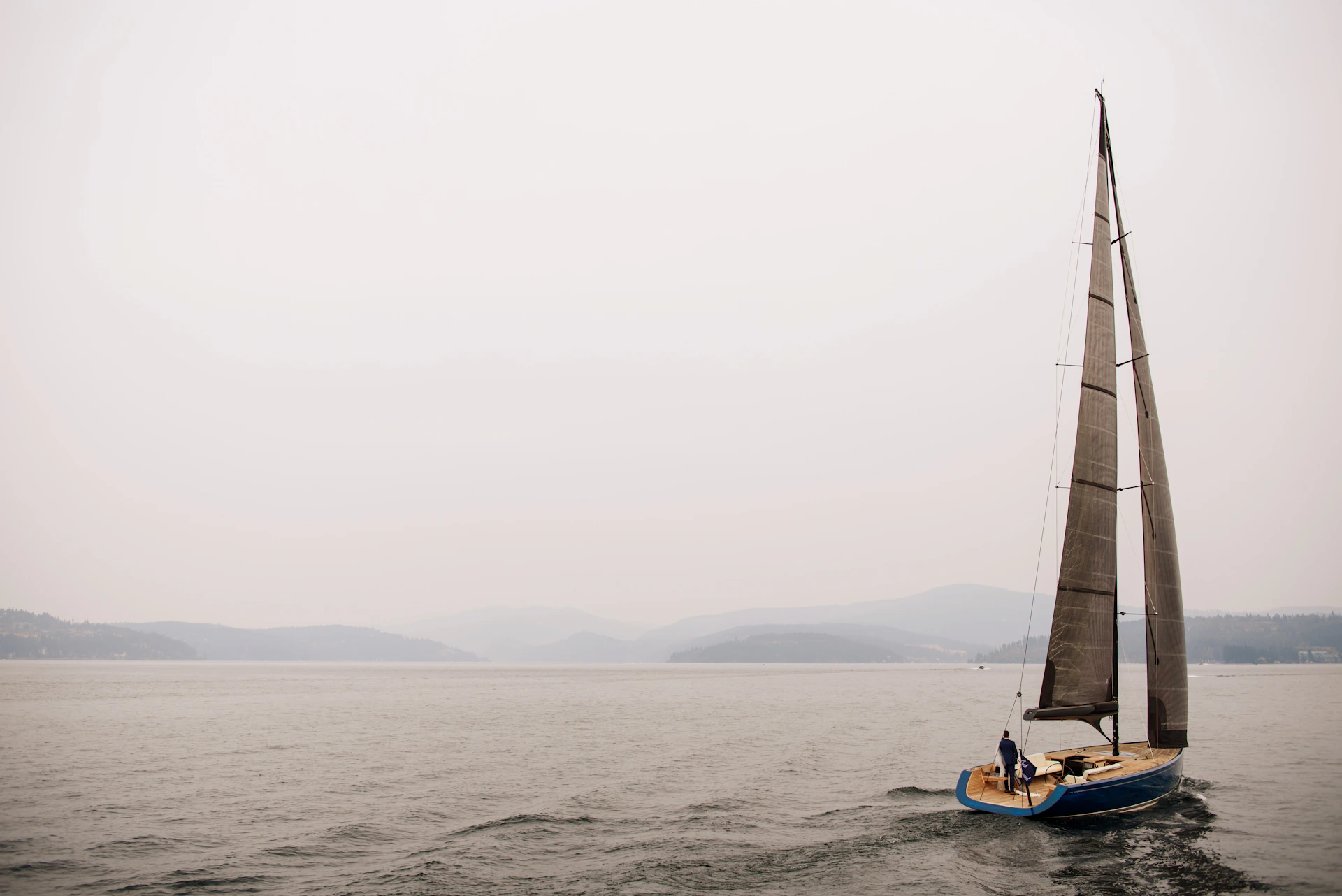 A candid moment from a sailing lesson, showing a captain guiding a guest’s hands on the ropes against a backdrop of calm lake waters.