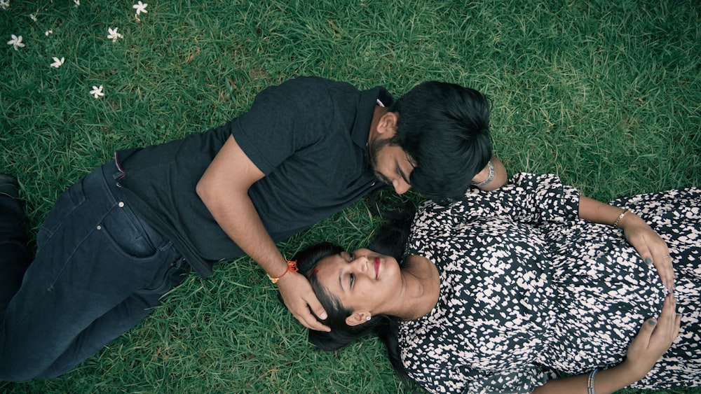 man in black crew neck t-shirt lying on green grass beside woman in black and