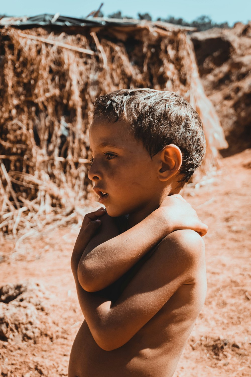 topless boy sitting on sand during daytime