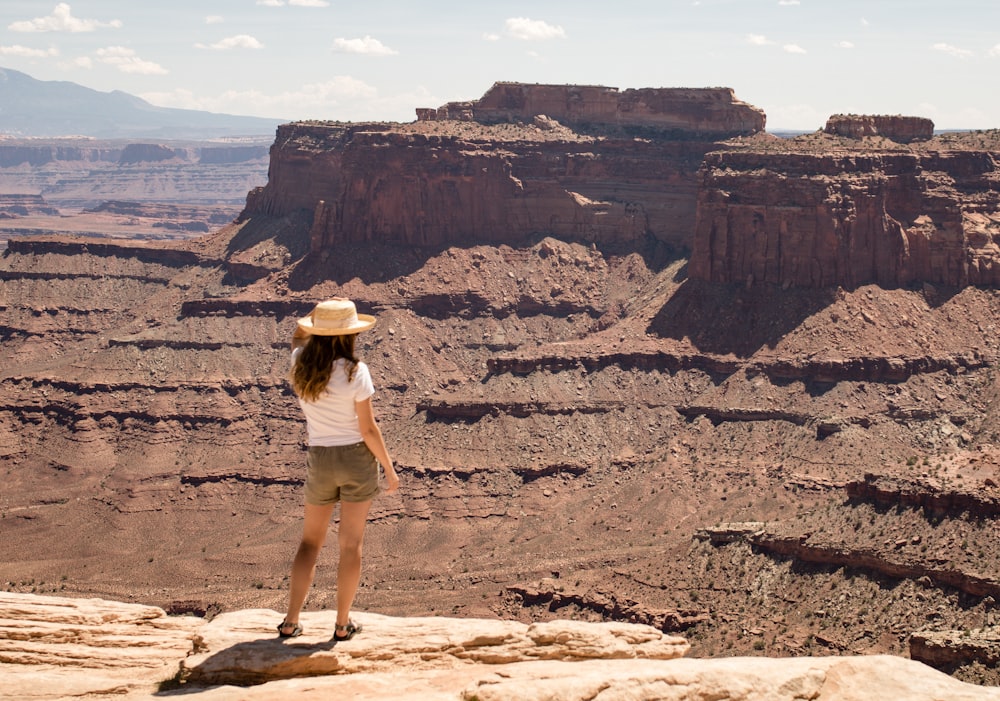 woman in white shirt and brown shorts standing on brown rock formation during daytime