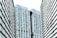 A modern urban architectural scene features high-rise buildings with a distinctive grid-like pattern. The skyscrapers have a mix of vertical and horizontal lines, creating an intricate façade. Singapore flags are displayed on the buildings, and greenery is integrated into the structure, reflecting urban planning and environmental considerations.