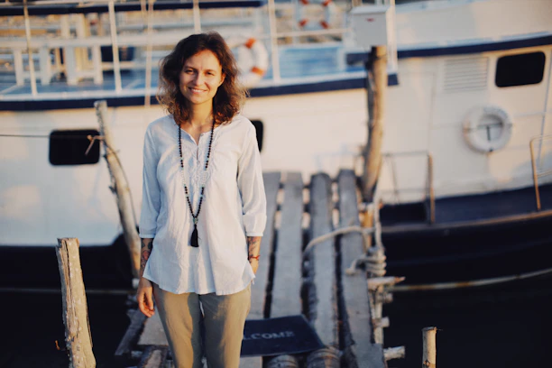 A smiling young professional holding a passport and cruise ship documents on a sunny dock.