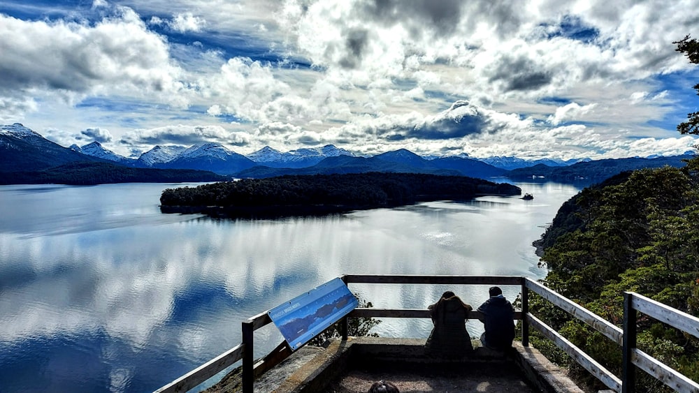 silhouette of 2 people sitting on wooden dock during daytime