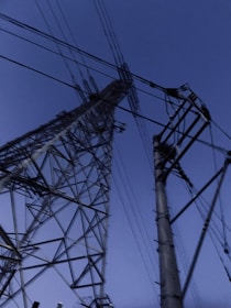 Large electrical transmission towers stretch upwards against a deep blue sky. The towers are composed of intricate metal frameworks and numerous power lines crisscross the scene.