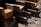 Stacks of large steel beams with yellow edges are arranged on a muddy construction site. The beams are layered in a repeating pattern and there are scattered rocks and debris on the ground.