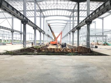 red and yellow heavy equipment on gray concrete ground under gray metal bridge during daytime