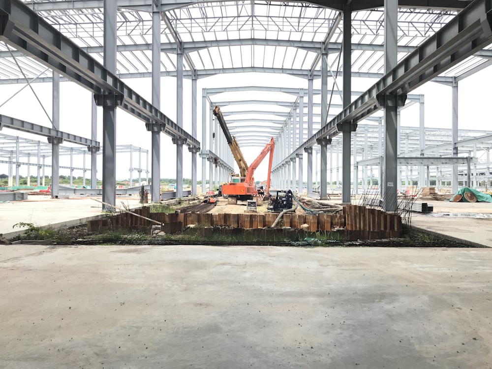 red and yellow heavy equipment on gray concrete ground under gray metal bridge during daytime