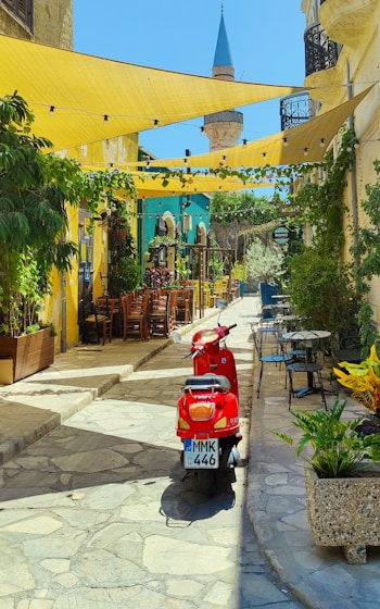 red motor scooter parked near yellow and blue concrete building during daytime