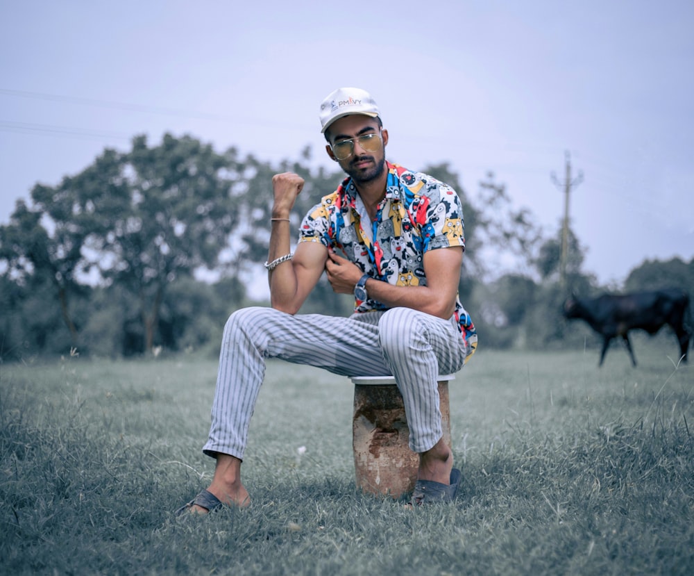 man in blue red and green floral button up shirt sitting on brown rock during daytime