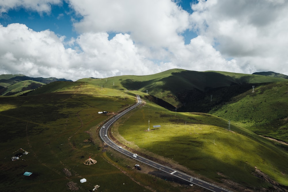 cars on road between green grass field under white clouds and blue sky during daytime