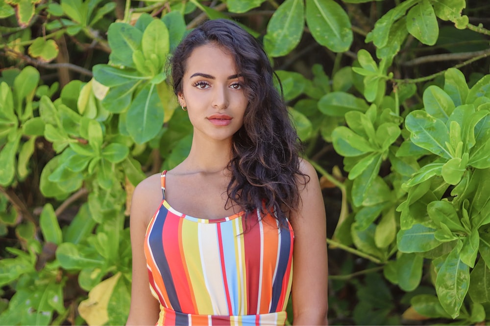 woman in white red and blue stripe tank top standing near green leaves