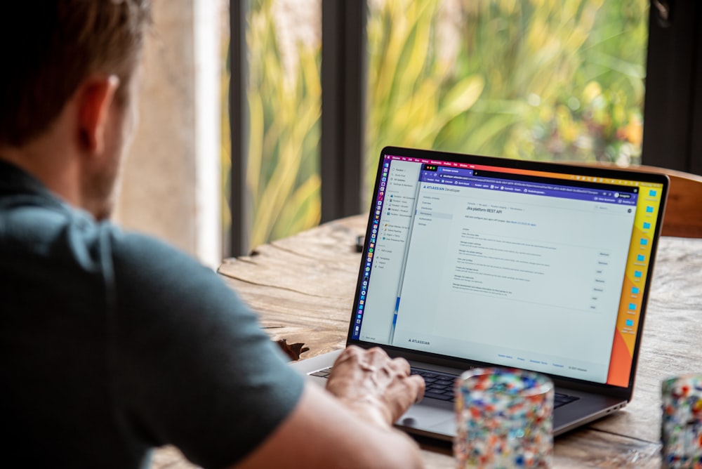 person using macbook pro on brown wooden table during daytime