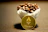 Close-up of a steaming cup of dark coffee with a bitcoin logo mug beside a laptop.
