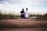 man and woman sitting on brown wooden pathway surrounded by green grass during daytime