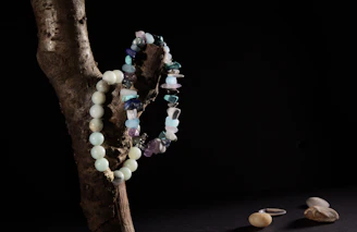 Close-up of a rugged necklace featuring deep blue lapis lazuli stones set in weathered silver, resting on driftwood by the sea.