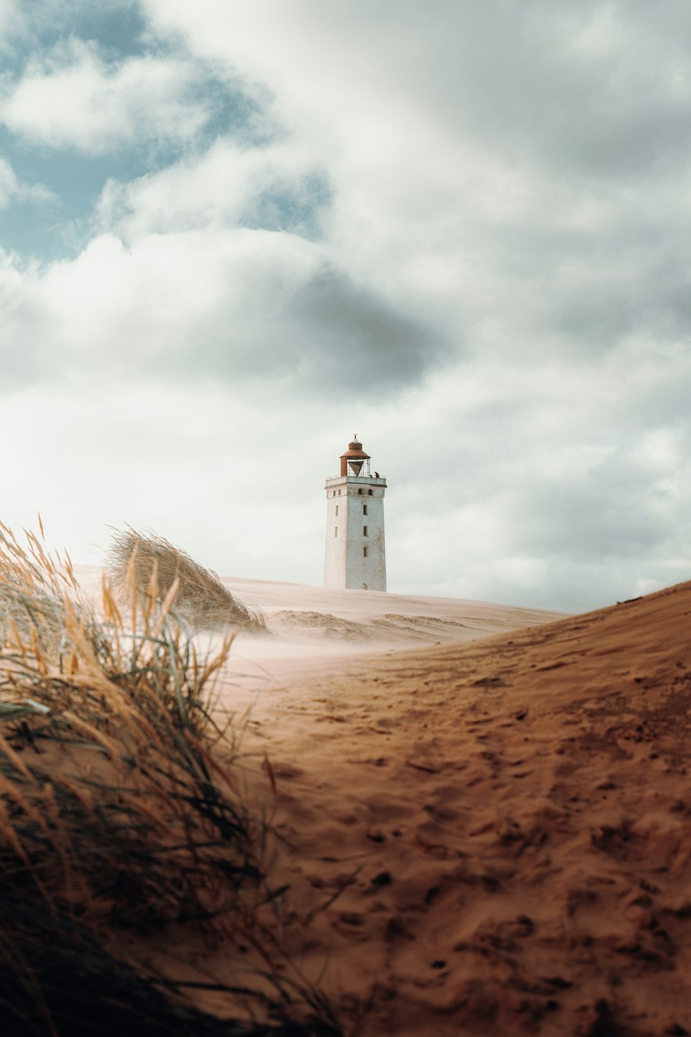 farol de concreto branco na areia marrom sob nuvens brancas durante o dia