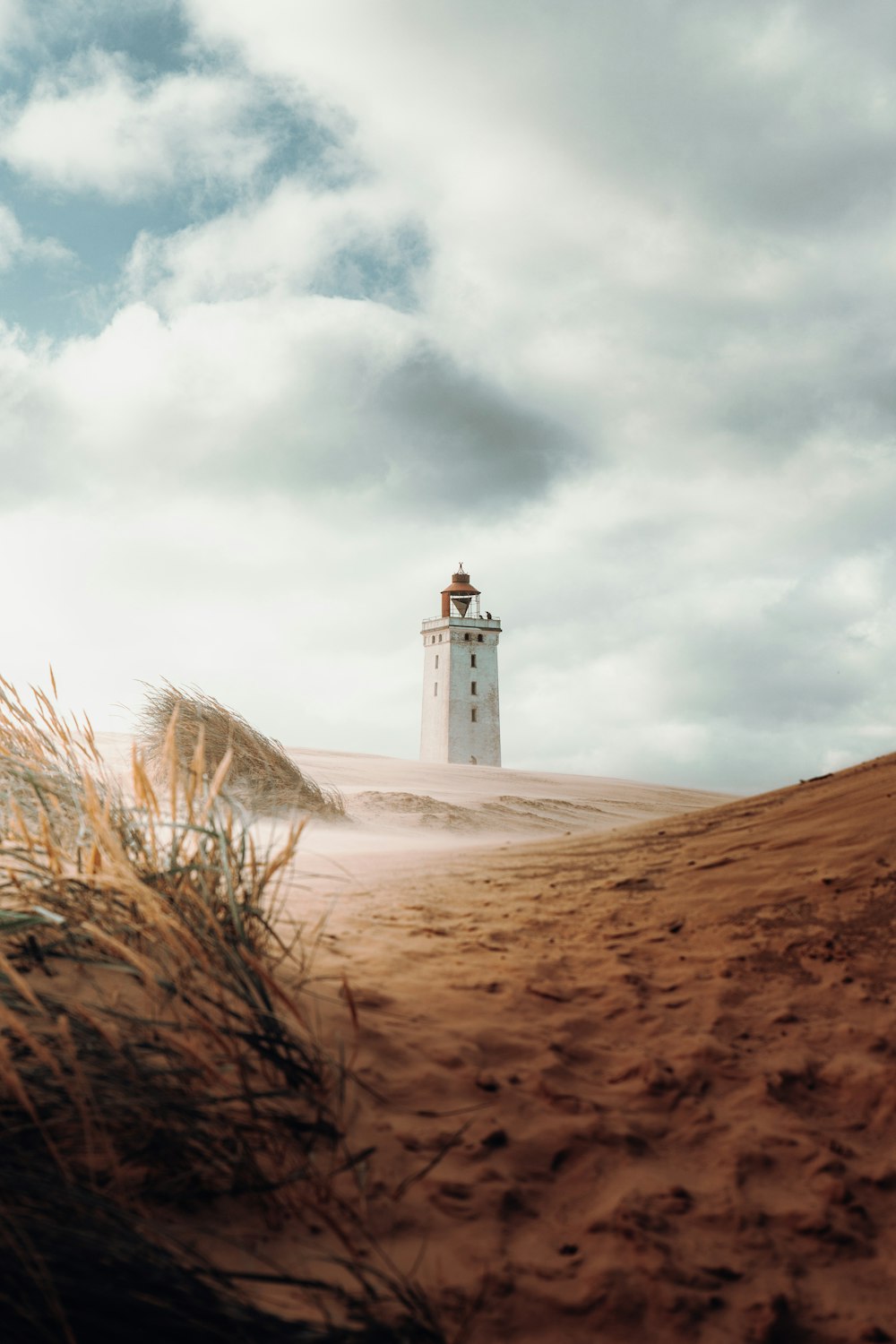 white concrete lighthouse on brown sand under white clouds during daytime