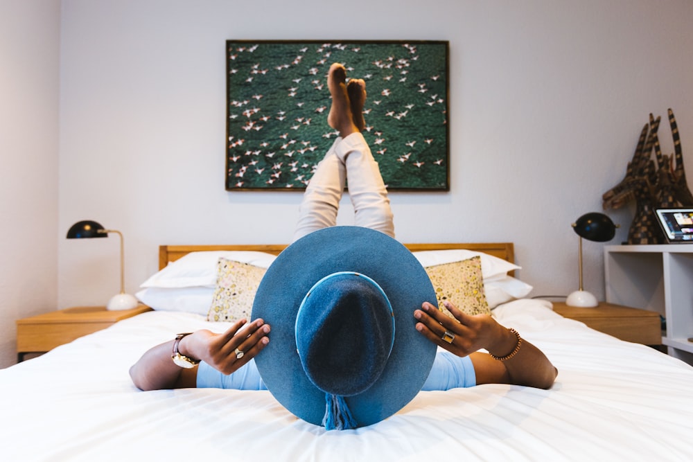 woman in blue tank top and white pants lying on bed