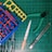 A collection of hobby tools and plastic model parts arranged on a green cutting mat with a grid pattern. The items include plastic model sprues in blue, red, and yellow, a metal file with an orange handle, green-handled clippers, and a utility knife.