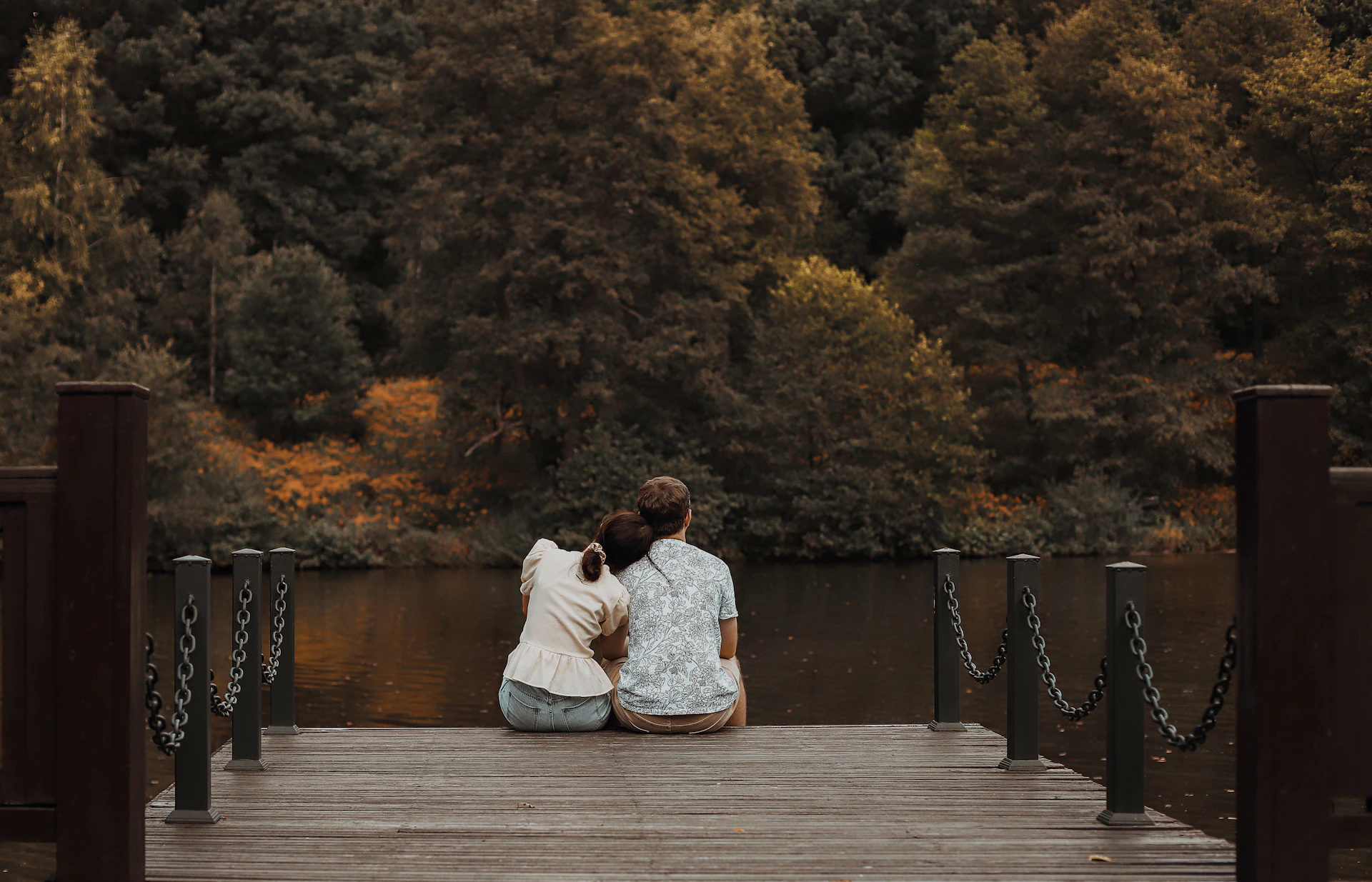 A couple enjoying a peaceful moment on a wooden deck overlooking a serene lake surrounded by lush forest.