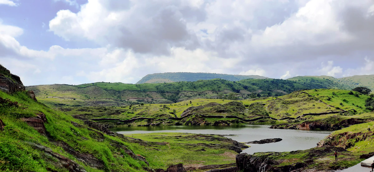 Green grass by a lake under a cloudy sky