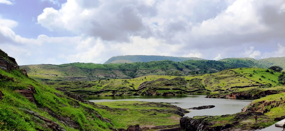 green grass field near body of water under cloudy sky during daytime