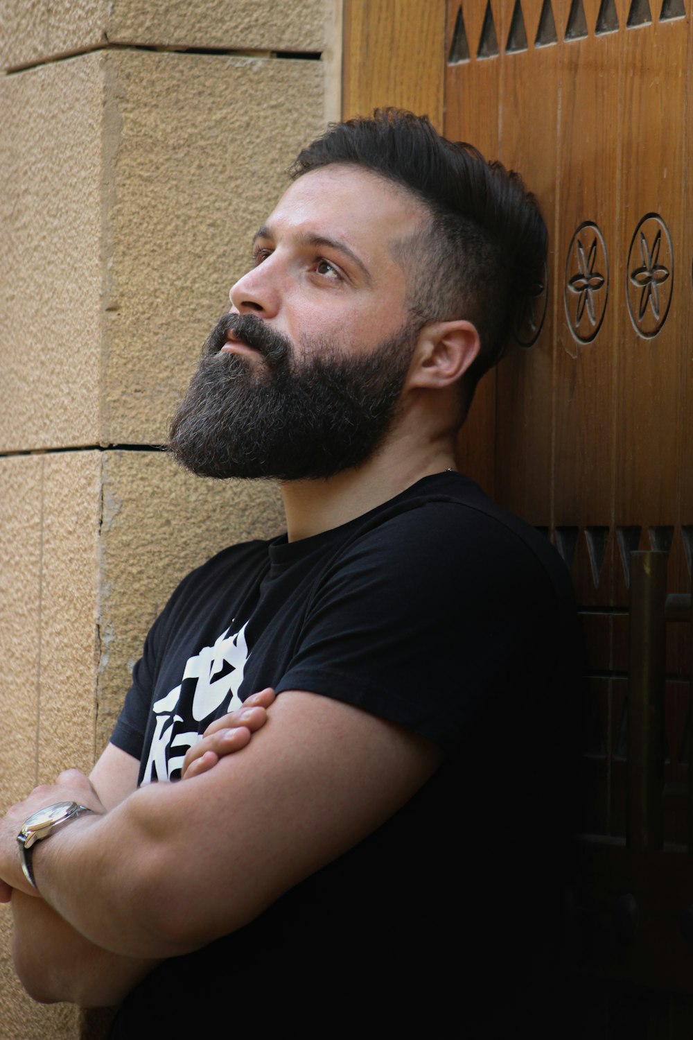 hombre con camiseta negra de cuello redondo sentado junto a la puerta de madera marrón