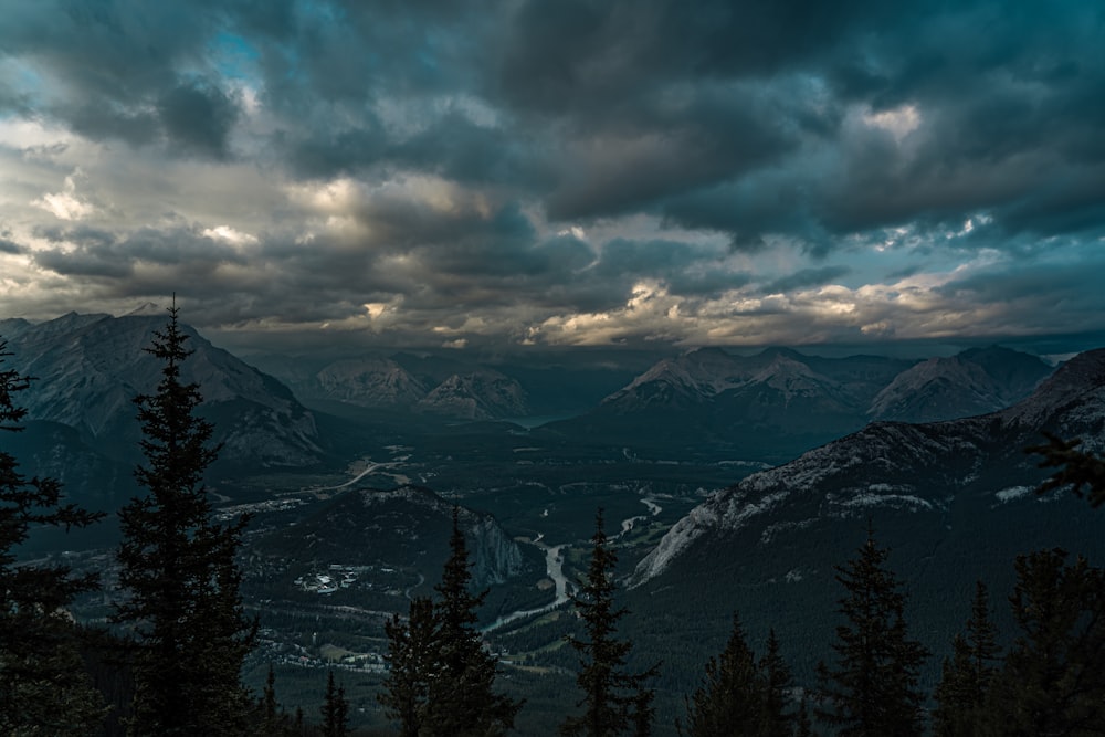 green pine trees near snow covered mountains under cloudy sky during daytime